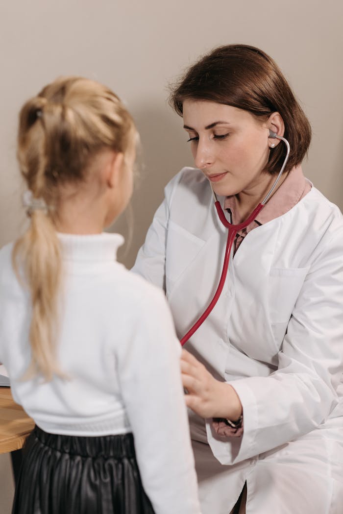 A female doctor examining a child with a stethoscope during a pediatric check-up in a clinic.